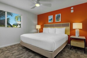Une chambre d’hôtel avec un lit, deux tables de chevet, un ventilateur de plafond et une fenêtre avec des stores.