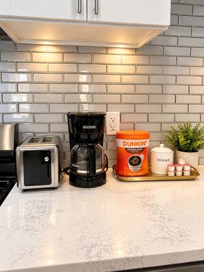 A kitchen counter with a toaster, a coffee maker, a Dunkin' coffee container, and a sugar container.