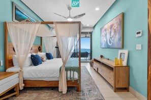 Ein Schlafzimmer mit Himmelbett, Deckenventilator, Blick ins Freie und einem Gemälde an der Wand.
