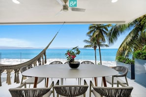 Ein runder Tisch mit sechs Stühlen, einer Topfpflanze und Blick auf Strand und Meer.