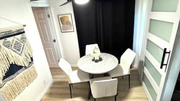 Un coin repas comprenant une table ronde et quatre chaises, un luminaire fixé au mur et une porte dotée d’un panneau en verre dépoli.