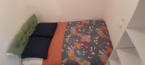 Ein Bett mit einem blumigem Überwurf, einem grünen Kopfkissen und einem dunkelblauen Kopfkissen.