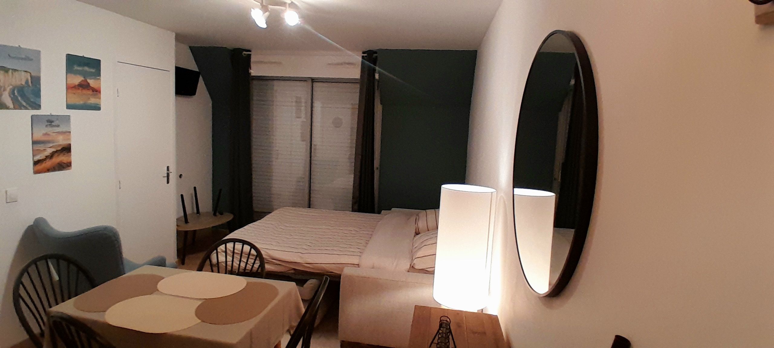 A bedroom with a bed, a desk, a chair, a table, a mirror, and artwork on the wall.