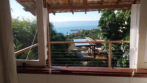 A balcony with a view of a coastal landscape, including a body of water and distant hills. - House with ocean view in Ilhabela (Ilhabela)