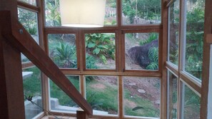 A view through a window with a wooden frame, looking out to a garden with various plants and a rock formation. - House with ocean view in Ilhabela (Ilhabela)