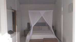 Een eenpersoonsbed met hemelbed, een nachtkastje en een bijzettafeltje.