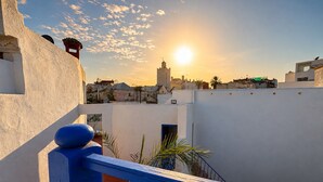 A rooftop with a blue railing, a view of the cityscape, and a sunset in the background. - Wonderful 3-bedroom riad with AC in charming Azemmour (Azemmour)