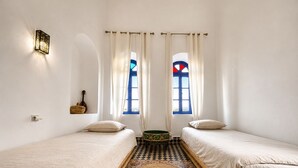 A room with two beds, a patterned floor, a wall-mounted light fixture, and a window with curtains. - Wonderful 3-bedroom riad with AC in charming Azemmour (Azemmour)