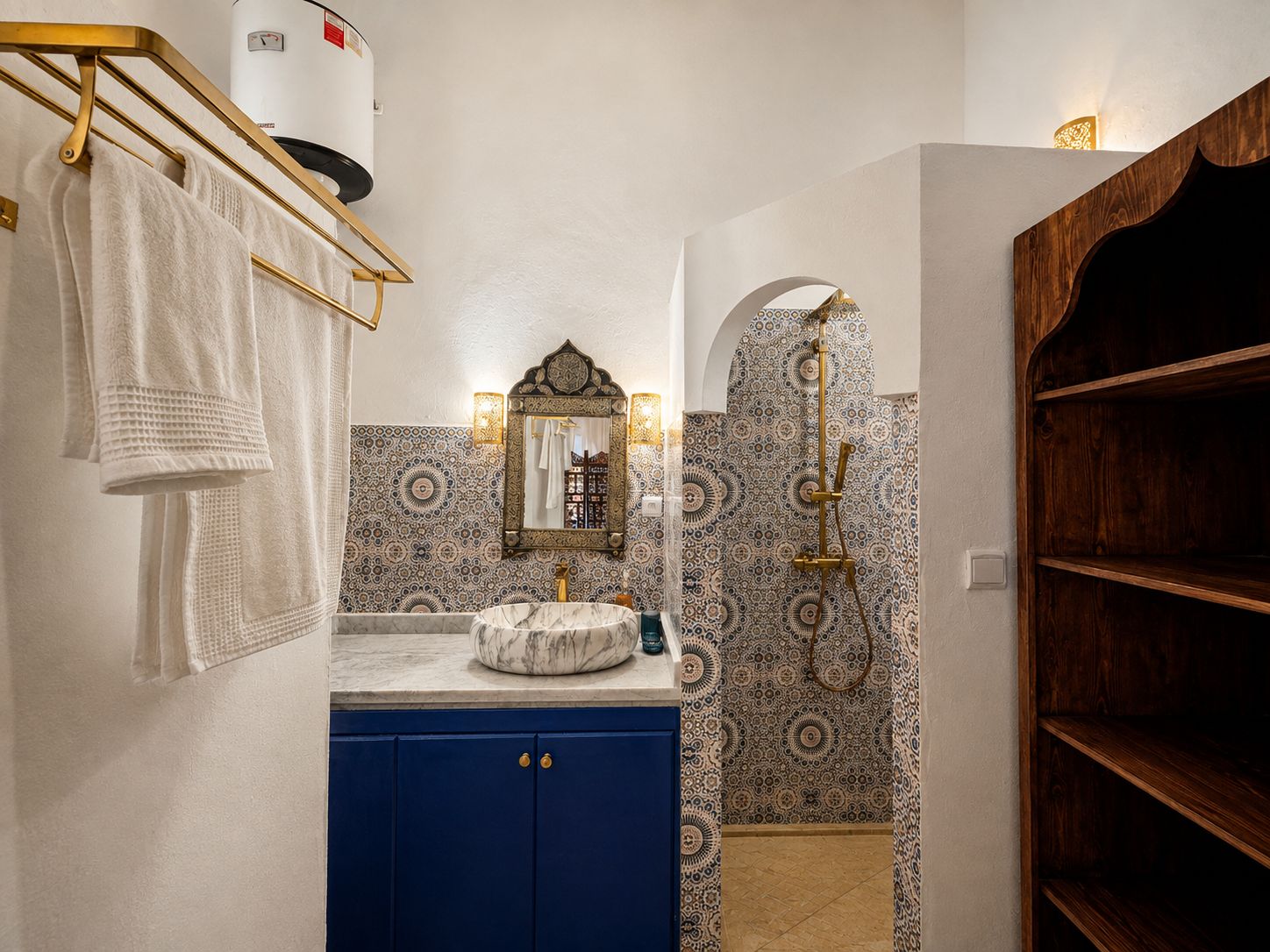 Une salle de bain avec un lavabo en marbre, un meuble bleu, des carreaux à motifs et une étagère en bois.