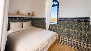 A bedroom with a bed, a window with a view, a shelf with decorative items, and patterned tile walls. - Wonderful 3-bedroom riad with AC in charming Azemmour (Azemmour)