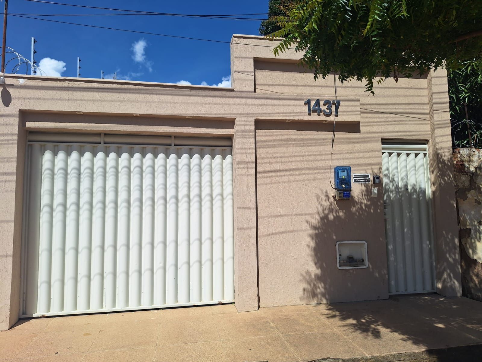 A beige building with a garage door, a number '1437' sign, and a small window with a security device.