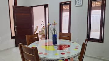 Un comedor con una mesa redonda, sillas, un florero con flores y un reloj en la pared.