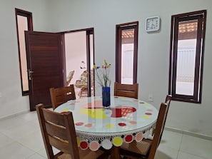 A dining area with a round table, chairs, a vase with flowers, and a clock on the wall. - Casa linda em bairro nobre (JUAZEIRO DO NORTE)