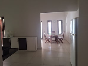 A kitchen with a dining table, chairs, a refrigerator, and a countertop with appliances.