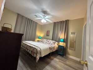 Ein Schlafzimmer mit einem Bett, zwei Nachttischlampen, einem Deckenventilator und einer Tür.