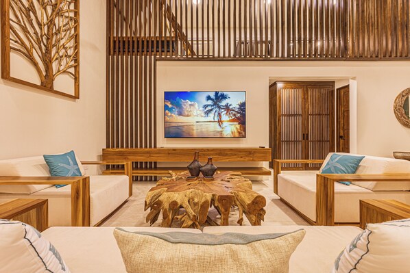 A modern living room with a large flat-screen TV, wooden furniture, and a decorative tree branch wall art piece.