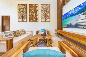 A modern living room with a wooden coffee table, a sofa with patterned cushions, and a large flat-screen TV mounted on the wall. - Luxury 3-Bedroom Villa with Private Pool, 100m from Playa Matapalo (Savegre)