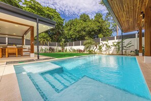 A modern outdoor swimming pool with a wooden deck and a covered seating area.