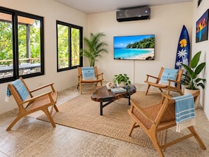 Ein Zimmer mit großem Fernseher, Korbsesseln, einem Couchtisch und Blick auf einen tropischen Strand.