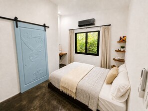 Une chambre à coucher comprenant un lit, une porte coulissante ornée de motifs floraux, une fenêtre avec des rideaux et un climatiseur fixé au mur.