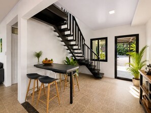 Un intérieur moderne avec un escalier, un coin repas avec des tabourets et une vue à travers une porte vitrée.