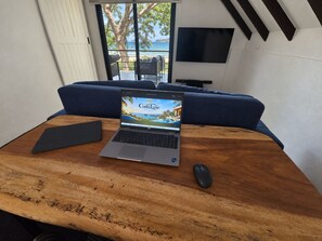Ein Laptop auf einem Holztisch mit Blick auf einen Balkon und einem an der Wand befestigten Fernseher.