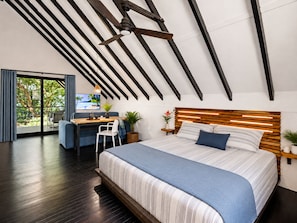 Ein modernes Schlafzimmer mit schrägem Dach, einem großen Bett mit Holz-Kopfstütze, einem Schreibtisch mit Stuhl und Blick durch eine Glastür.