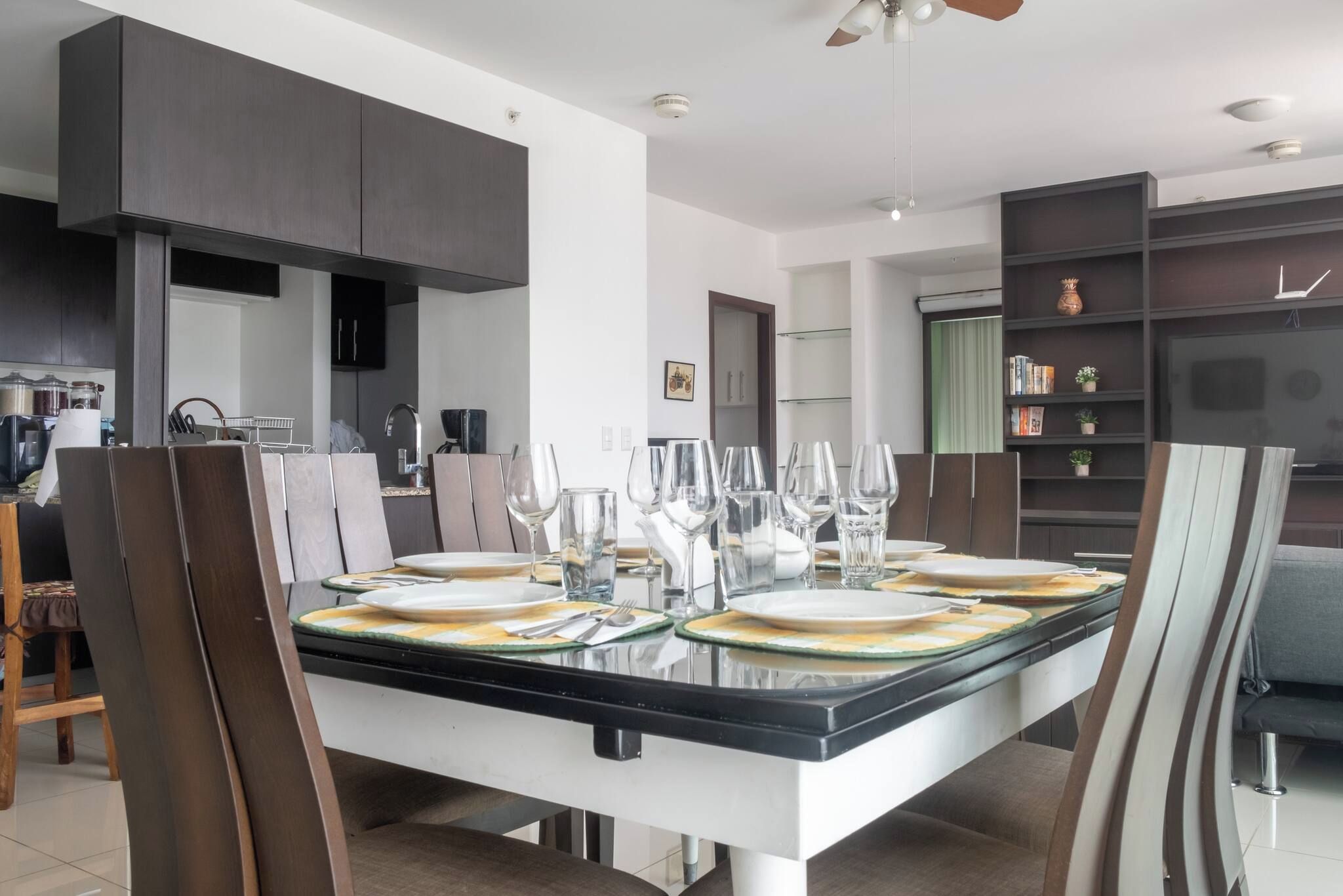 Un espace repas moderne avec une table à plateau de verre pouvant accueillir six personnes, entourée de chaises en bois foncé.