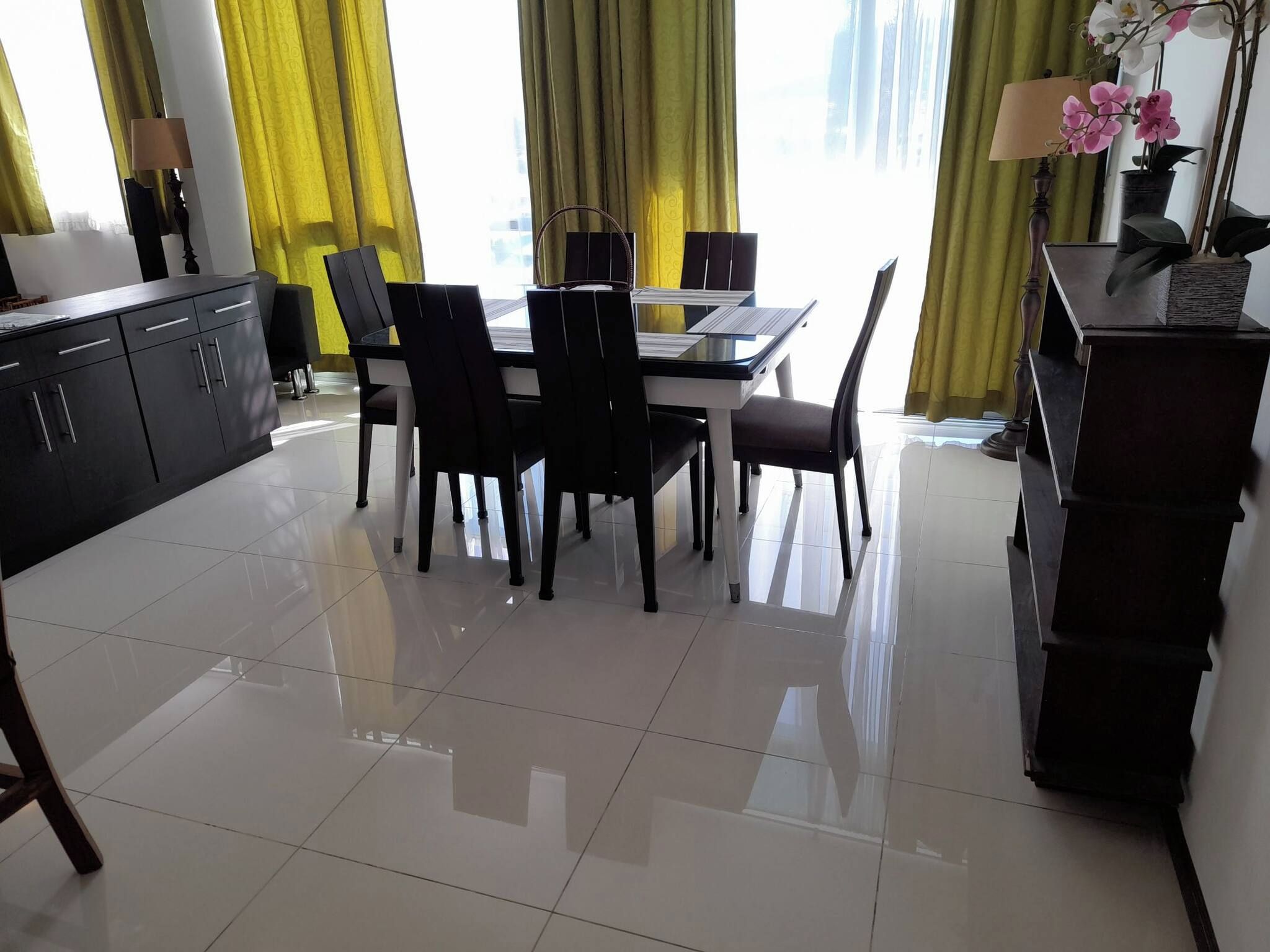 A modern dining area with a glass table, black chairs, and yellow curtains.