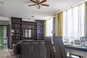 A modern living room with a flat-screen TV, dark wood furniture, and a dining area with chairs and a table set for a meal.