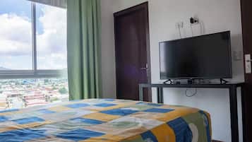 Une chambre d’hôtel avec un lit, un téléviseur posé sur un meuble, une fenêtre avec des rideaux et une porte.