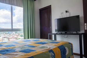 Une chambre d’hôtel avec un lit, un téléviseur posé sur un meuble, une fenêtre avec des rideaux et une porte.