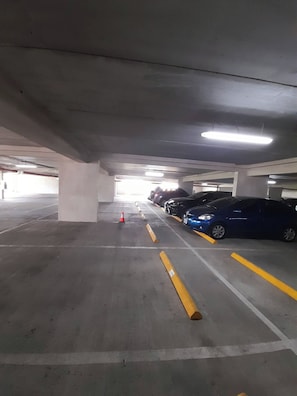Garagem subterrânea com pilares de concreto, iluminação fluorescente e vagas demarcadas.