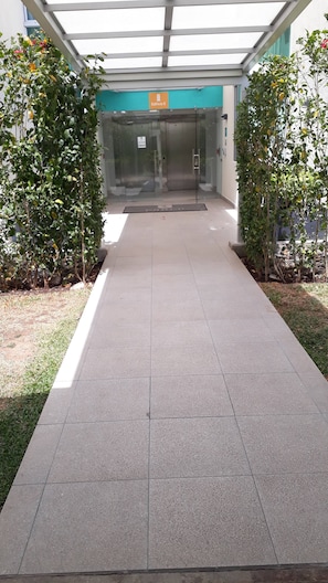 A pathway leading to a building entrance with a glass door, a sign above indicating 'Edificio E', and a clear sky above.