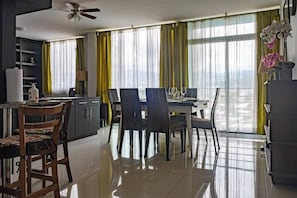 A modern dining area with a table set for four, a kitchen area with a refrigerator, and a view through large windows.