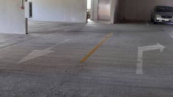 Ett tomt parkeringsgarage med betonggolv, riktningspilar och en bil som står parkerad en bit bort.