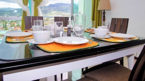 Una mesa de comedor dispuesta con platos, tazones y vasos blancos, con vistas a montañas al fondo.