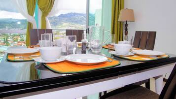 Una mesa de comedor dispuesta con platos, tazones y vasos blancos, con vistas a montañas al fondo.