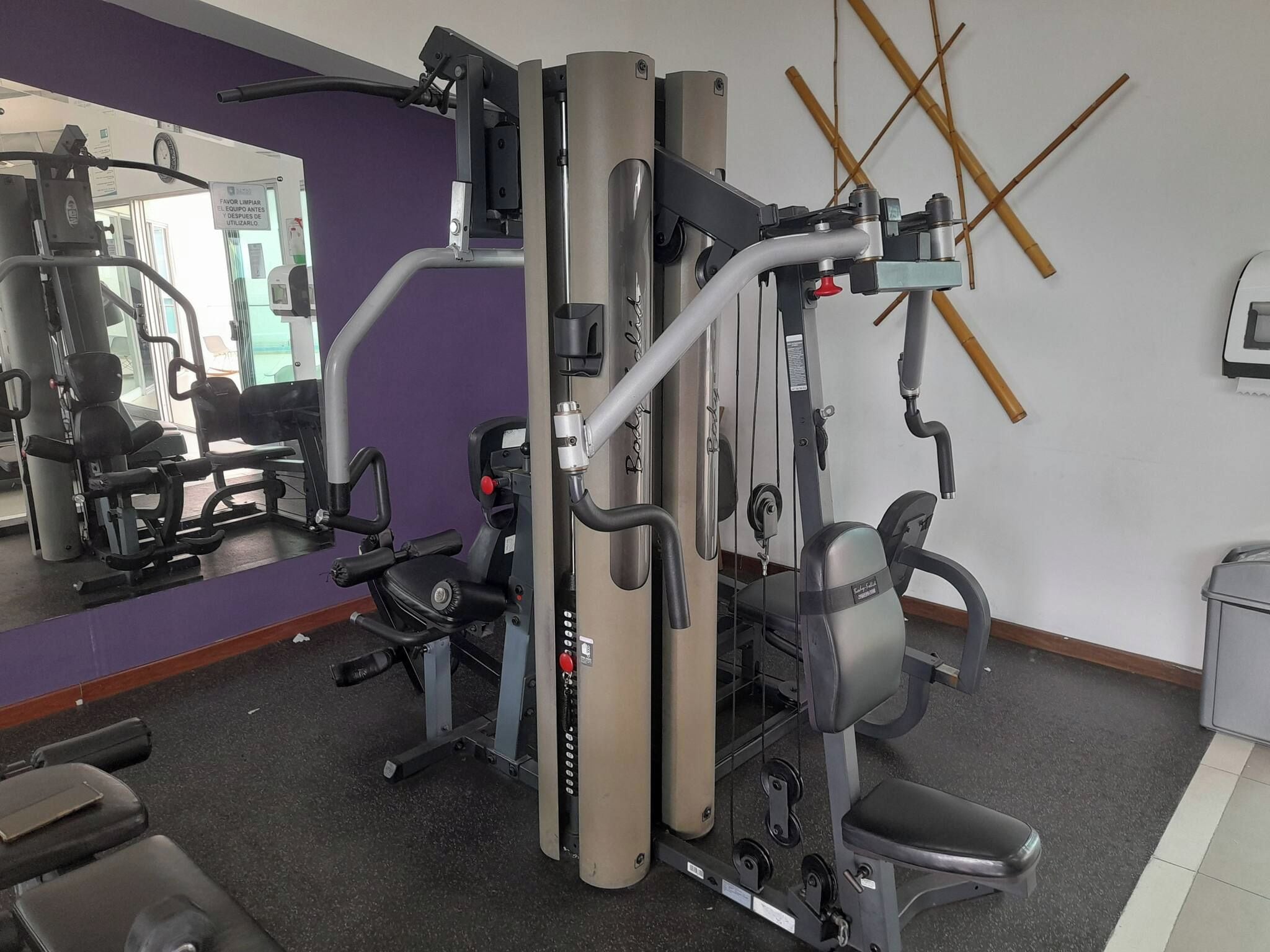 A gym with various exercise machines, a mirror, and a wall with a clock.