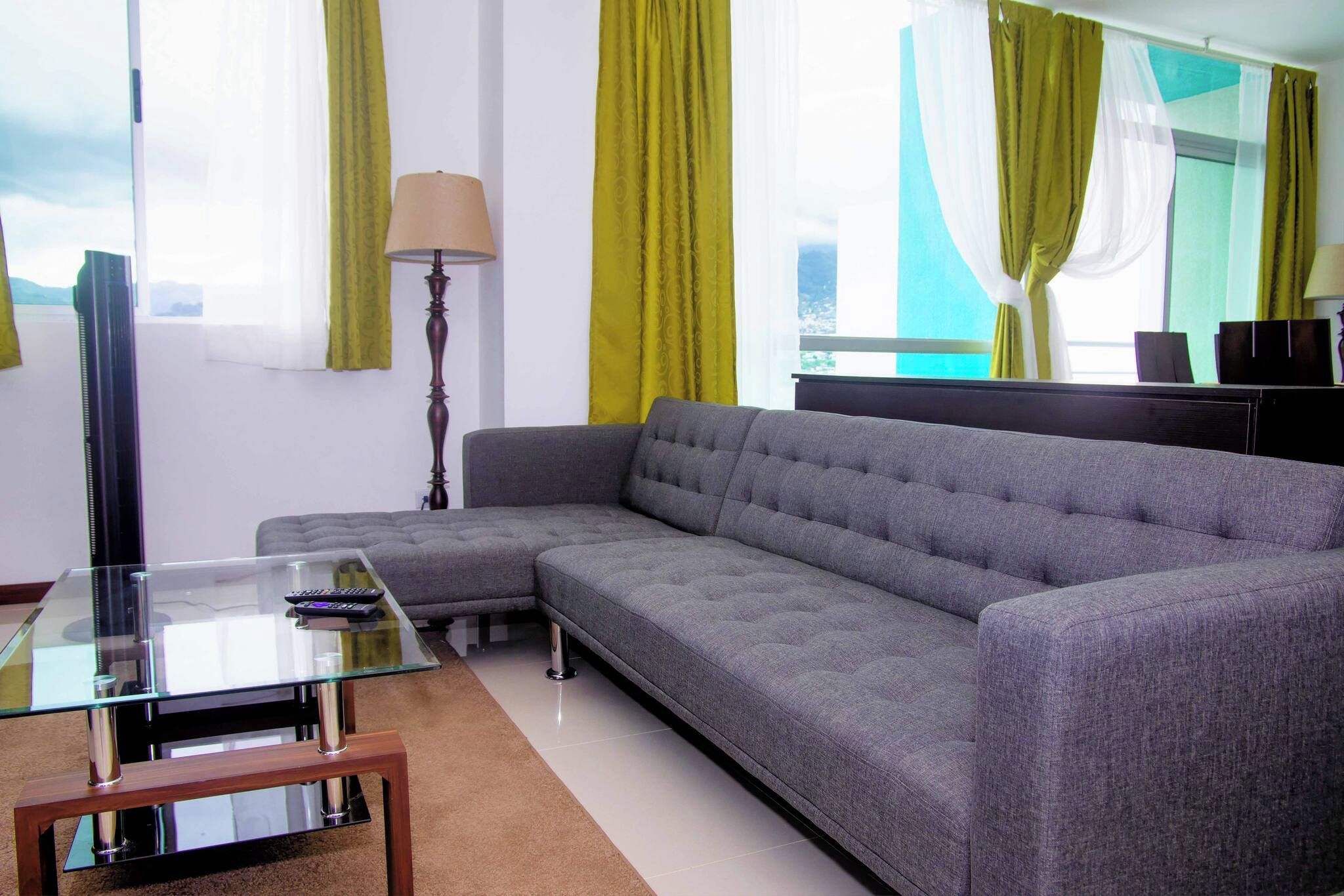 Una sala de estar moderna con un sofá seccional, una mesa de centro de vidrio y una lámpara.