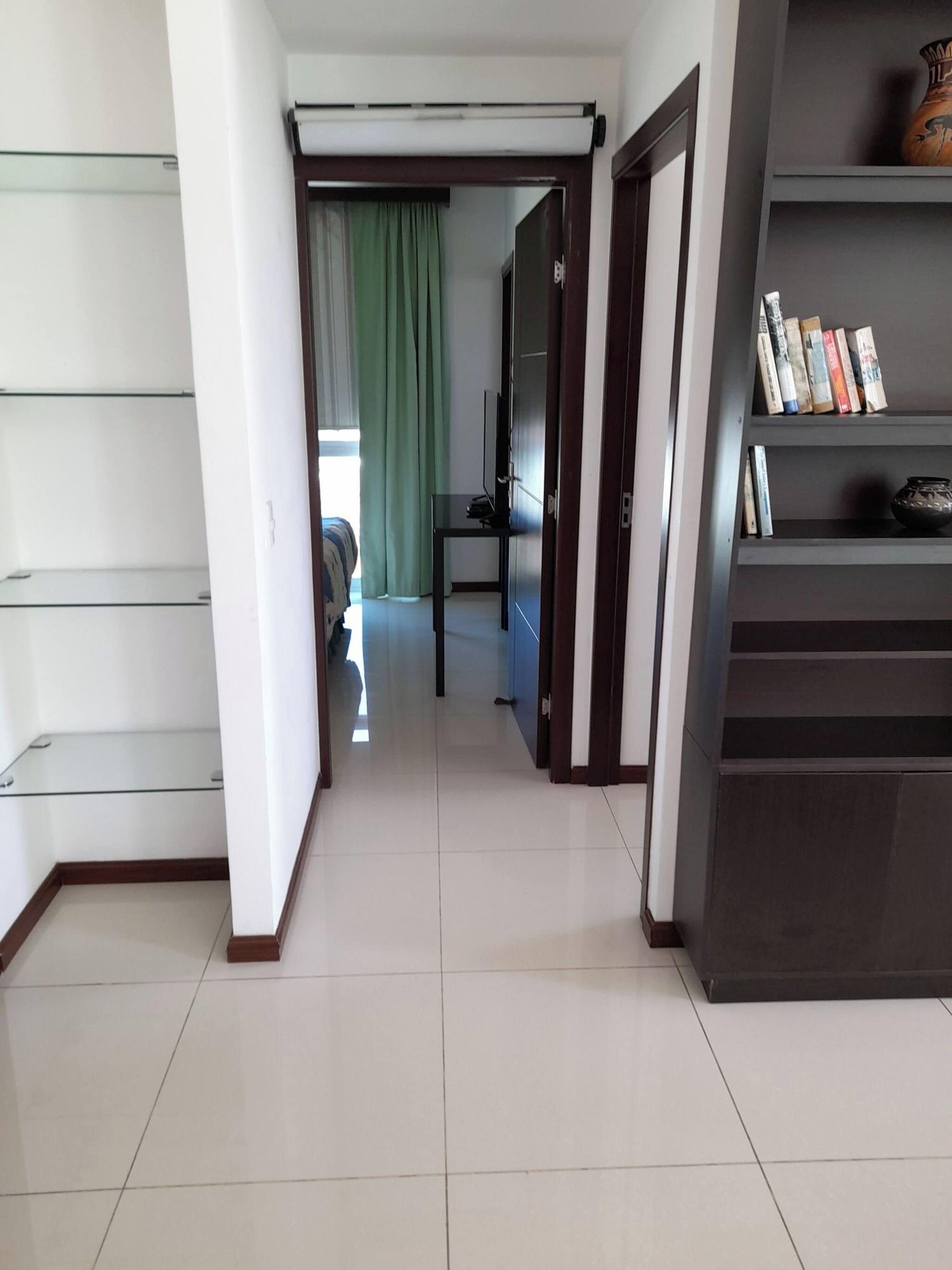 Un pasillo con una puerta de vidrio, una estantería llena de libros y un televisor sobre un soporte.