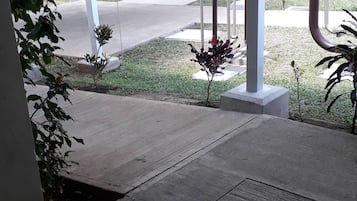 A covered outdoor area with a concrete floor, a metal bench, and a small garden with plants.