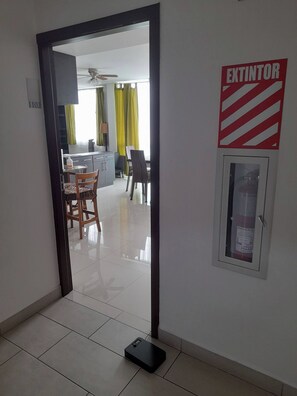A hallway with a fire extinguisher mounted on the wall, a door leading to a dining area, and a small table with chairs.