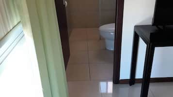 Une chambre d’hôtel avec un lit, une salle de bain comprenant des toilettes et une douche, et une fenêtre avec des rideaux.
