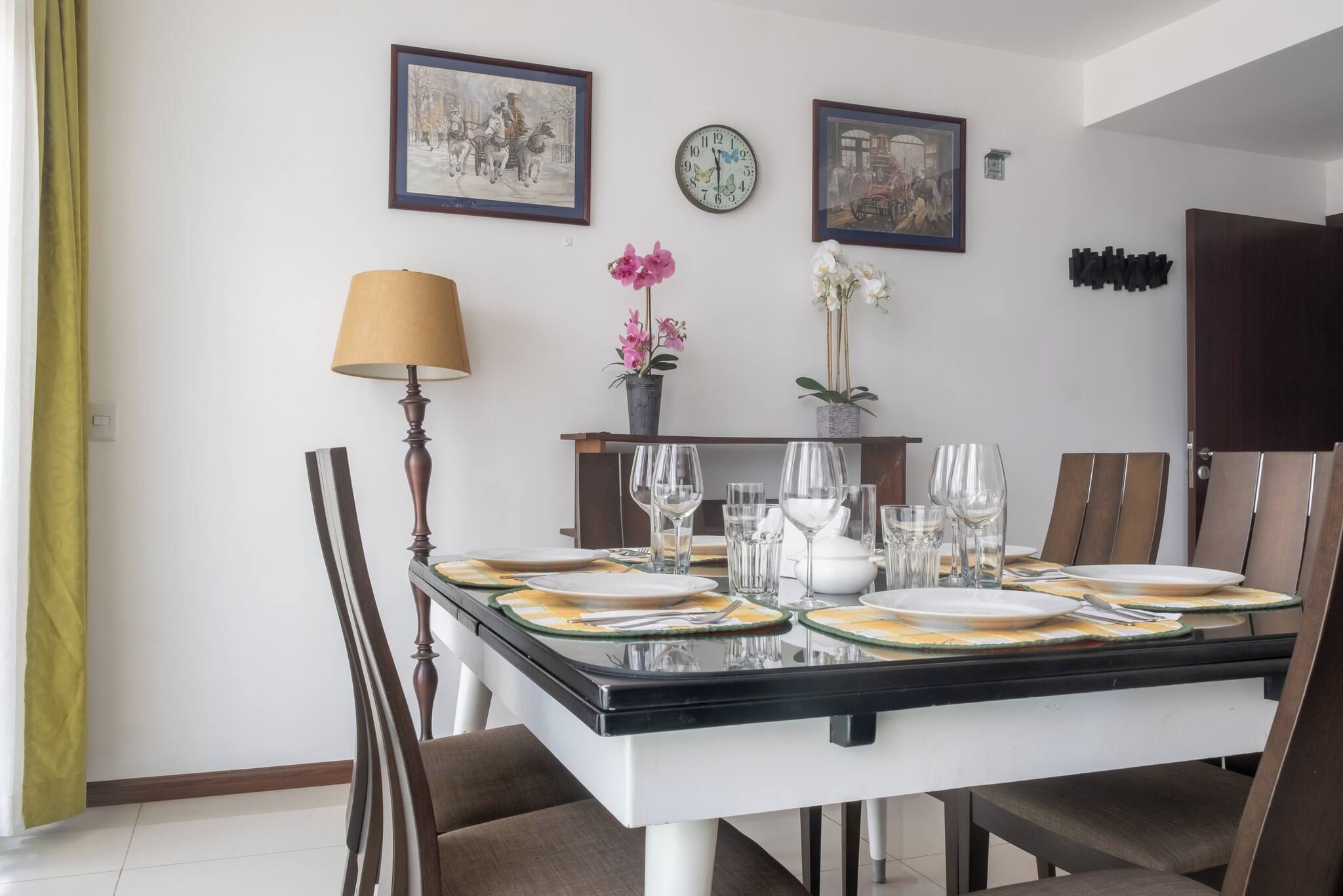 Comedor con mesa dispuesta para seis, sillas, lámpara y relojes en la pared.