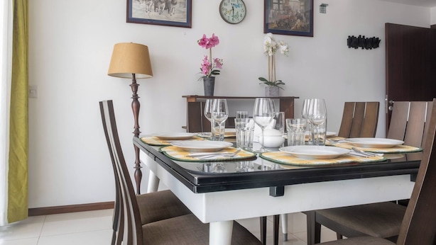 Comedor con mesa dispuesta para seis, sillas, lámpara y relojes en la pared.