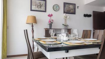Comedor con mesa dispuesta para seis, sillas, lámpara y relojes en la pared.