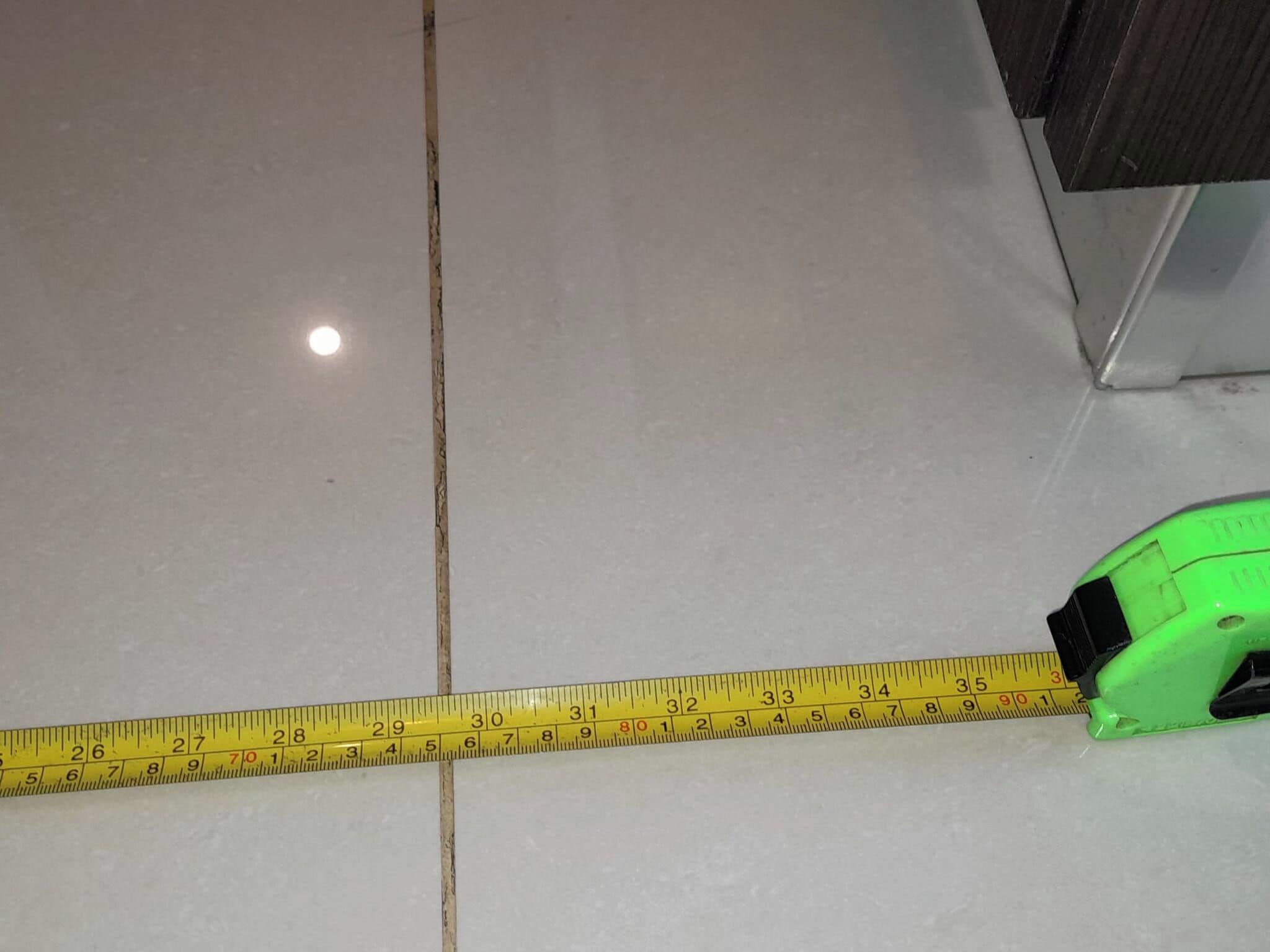 A yellow measuring tape laid out on a floor with a visible crack.