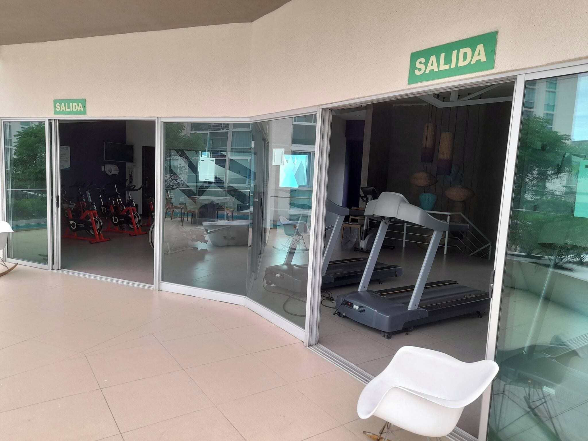 A fitness center with treadmills, a stationary bike, and a white chair. There are signs indicating an exit.