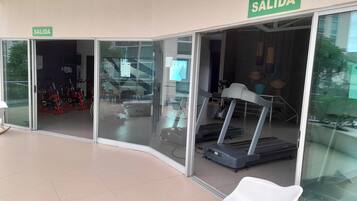A fitness center with treadmills, a stationary bike, and a white chair. There are signs indicating an exit.